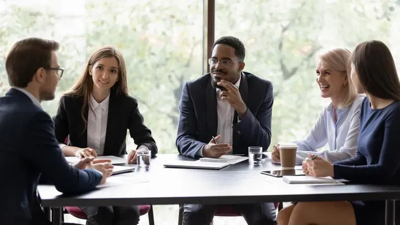 Five professionals in business attire collaborating at a conference table in a modern office